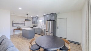 Una cocina moderna con gabinetes grises, un refrigerador de acero inoxidable y una zona de comedor con una mesa redonda y sillas de madera.
