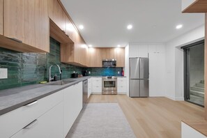 Eine moderne Küche mit Holzschränken, Edelstahlgeräten und einer grünen Spritzschutzwand.