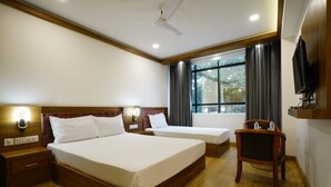 A hotel room with a large bed, a smaller bed, a wooden nightstand, a chair, a TV, and a window with curtains. - Hotel Astro Marine (Kanayannur)