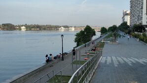A riverside walkway with benches and a railing, a bridge in the background, and a building with balconies. - Hotel Astro Marine (Kanayannur)