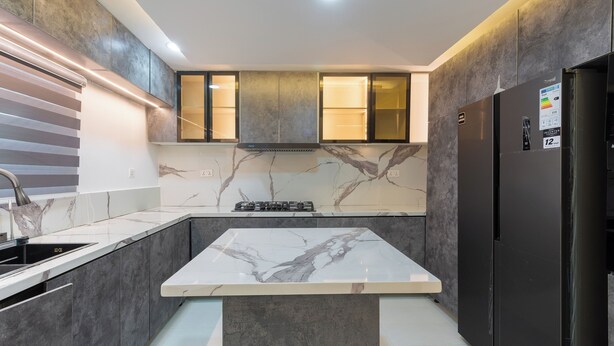 Une cuisine moderne dotée d’un îlot central, de meubles de rangement aux couleurs sombres et d’une cuisinière intégrée.