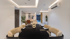 Un espace repas moderne avec une table noire, des chaises recouvertes d’un tissu beige et un éclairage encastré au plafond.