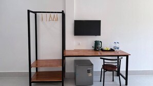 Une pièce de taille modeste, comprenant un bureau en bois, une chaise, un petit réfrigérateur et un téléviseur fixé au mur.