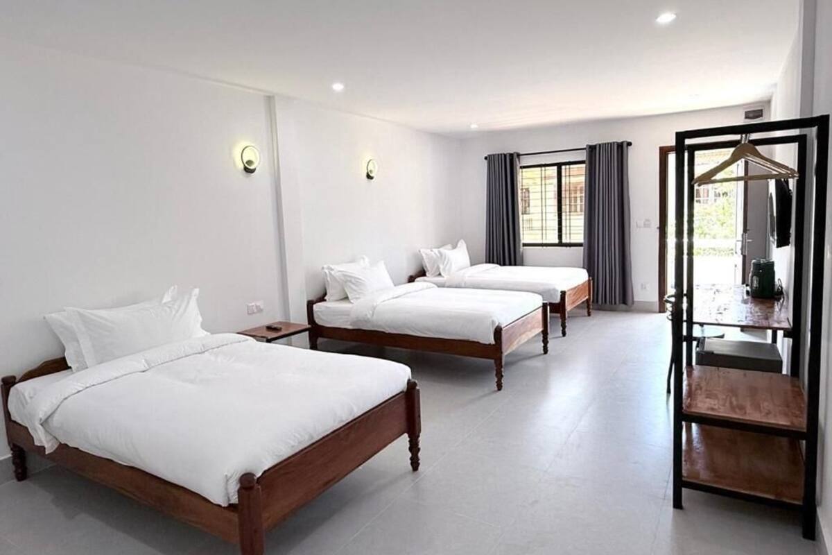 Una camera d'albergo con due letti di legno, un tavolino e un attaccapanni.