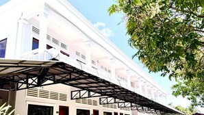 Un bâtiment blanc avec une allée couverte et un arbre au premier plan.