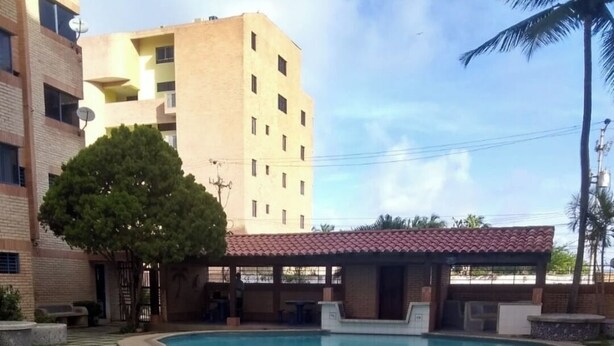 A swimming pool with a tiled deck, a covered seating area, and a building in the background. - Tucacas beach apartment (Tucacas)