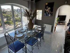 A dining area with a glass table, blue chairs, and a vase with dried plants. - CostaBlancaDreams - Studio 44 in Benissa (Benissa)