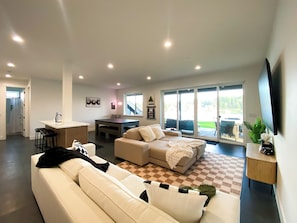 A modern living room with a sofa, a dining table, and a kitchen area with a bar. - Luxe Port Lookout with waterfront with dock, theater, hot tub, and huge deck (Kitsap County)