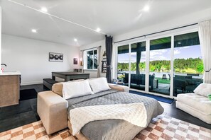 A bedroom with a bed, a desk, and a view of a green landscape through large windows. - Luxe Port Lookout with waterfront with dock, theater, hot tub, and huge deck (Kitsap County)
