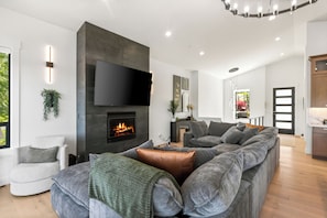 Una sala de estar moderna con chimenea, un sofá modular grande, un televisor de pantalla plana y una zona de comedor.