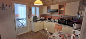 A compact kitchen with a refrigerator, microwave, stove, and sink. There is a window with a view of the outside, and a small table with chairs. - Spacious apartment, perfect for families and guests (Aouina)