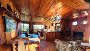 L’intérieur d’un chalet rustique comprend un coin repas, un canapé, une cuisine et une cheminée.