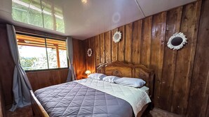 Une chambre aux murs lambrissés, avec un lit, des rideaux, une fenêtre et un miroir fixé au mur.