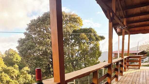 Une terrasse en bois avec une table, deux verres à vin et une bouteille de vin.