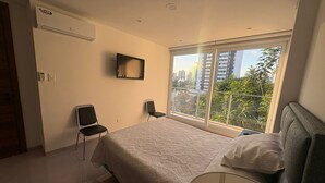 A bedroom with a bed, a chair, a TV, and a window with a city view. - Beutiful one bedroom one bathroom fully equiped apartment on the best zone of sc (Santa Cruz de la Sierra)
