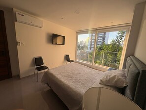 A bedroom with a bed, a chair, a TV, and a window with a city view. - Beutiful one bedroom one bathroom fully equiped apartment on the best zone of sc (Santa Cruz de la Sierra)