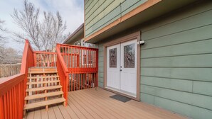 Una terraza de madera con barandilla roja, una puerta blanca y revestimiento verde en la casa.