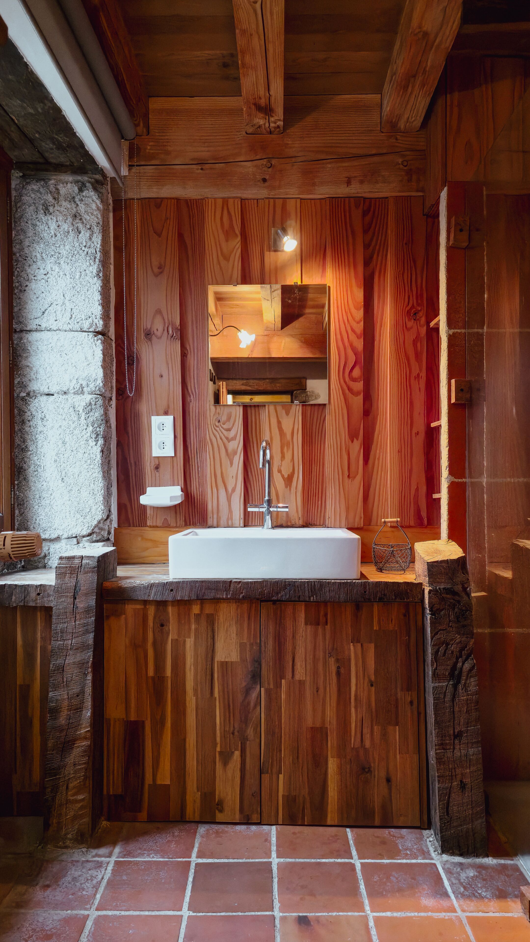 A rustic bathroom with a wooden vanity, a white sink, and a mirror.