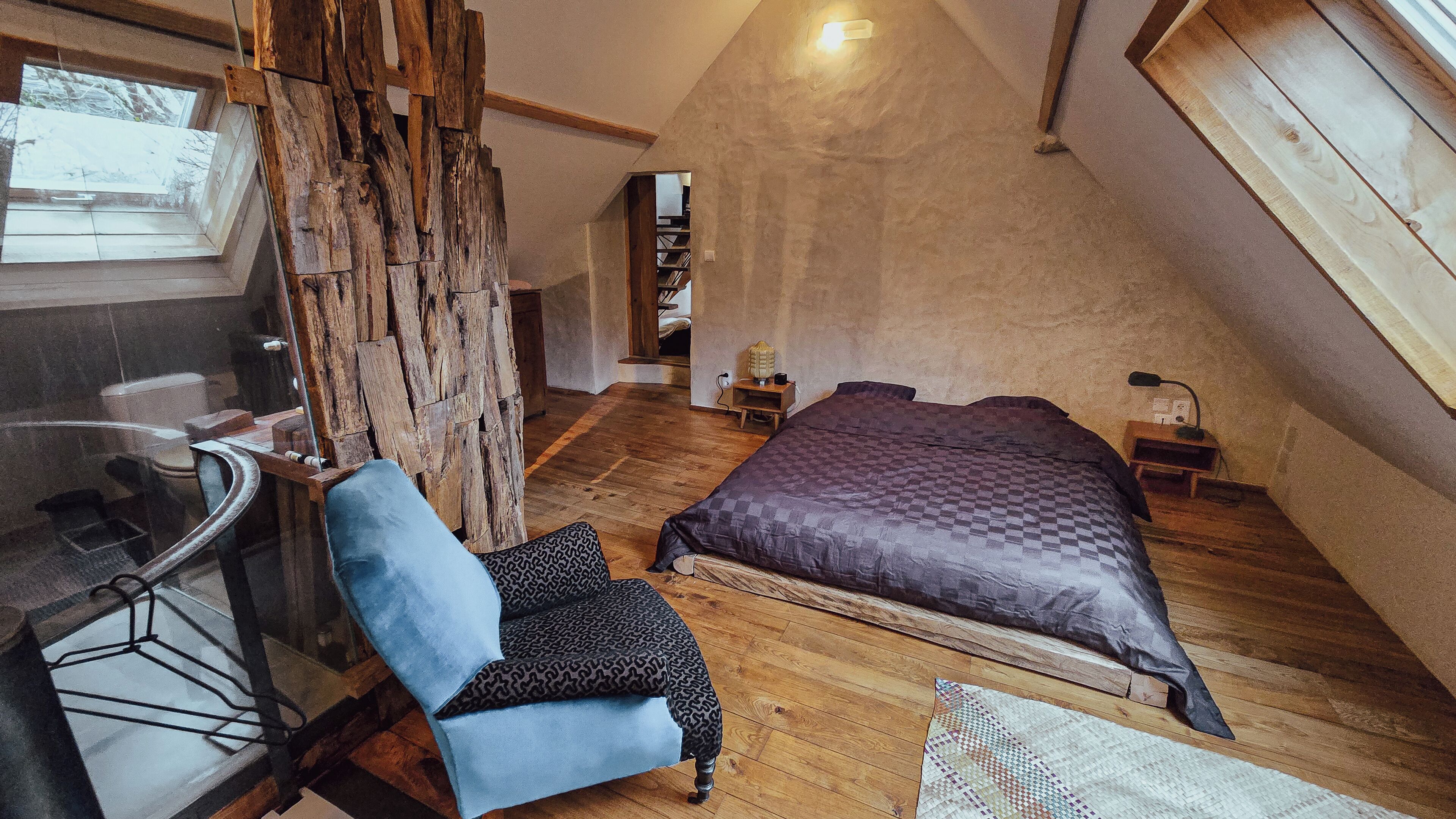 Une chambre située dans un espace de type « loft », avec un plafond en pente, un grand lit, une chaise, un mur en bois et une table en verre.