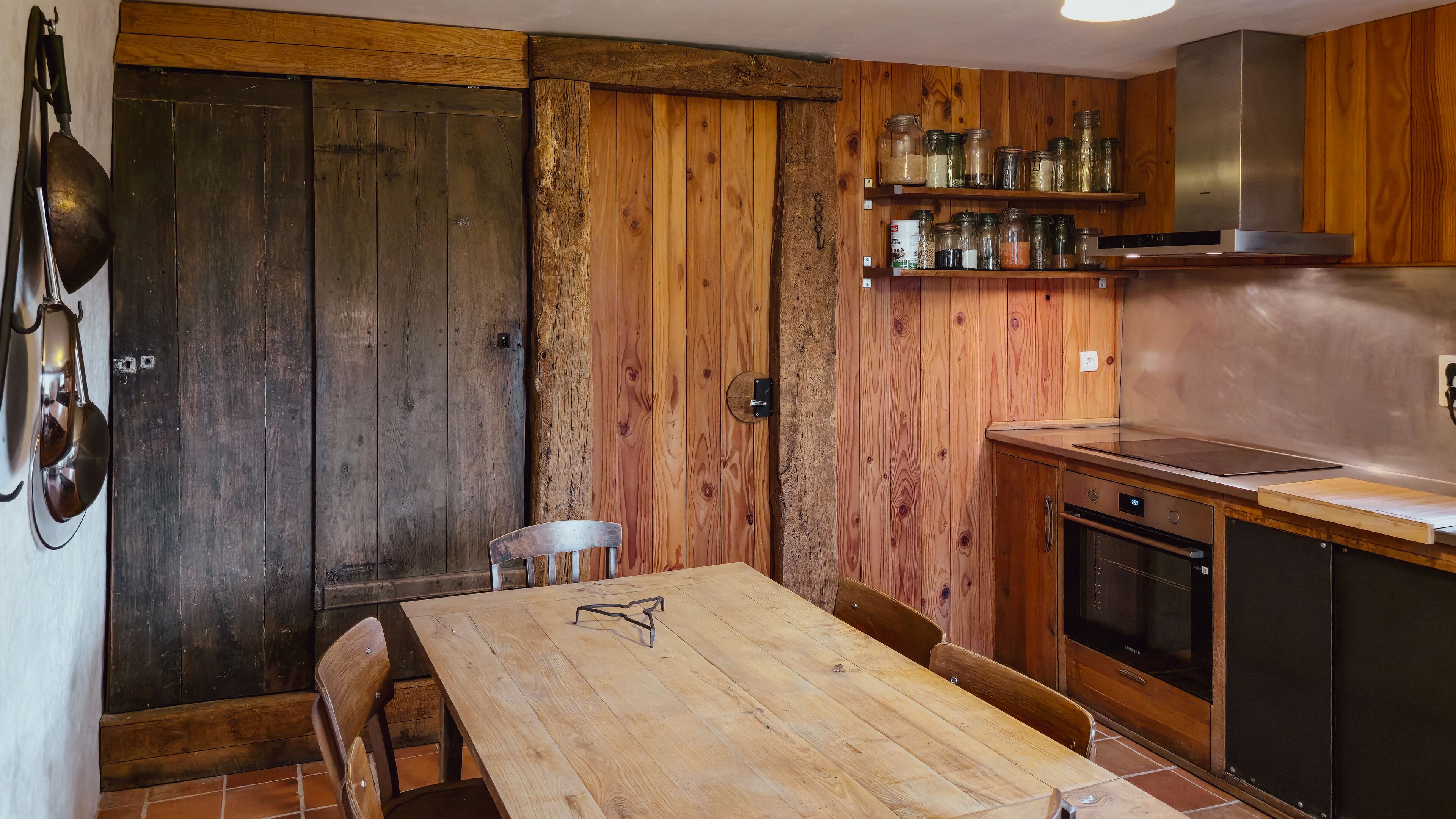 A rustic kitchen with wooden walls, a wooden table, and a built-in oven.