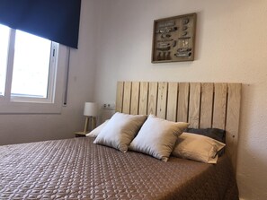 A bedroom with a wooden headboard, a quilted bedspread, two pillows, a bedside table with a lamp, and a wall-mounted display of various items. - AMSTERDAM. Exclusive Comfort on the Costa Brava (Roses)