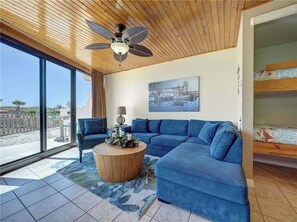 A modern living room with a sectional sofa, a round coffee table, a ceiling fan, and a large window offering a view of the beach. - Shared Heated Pool, Boardwalk to Beach (Corpus Christi)