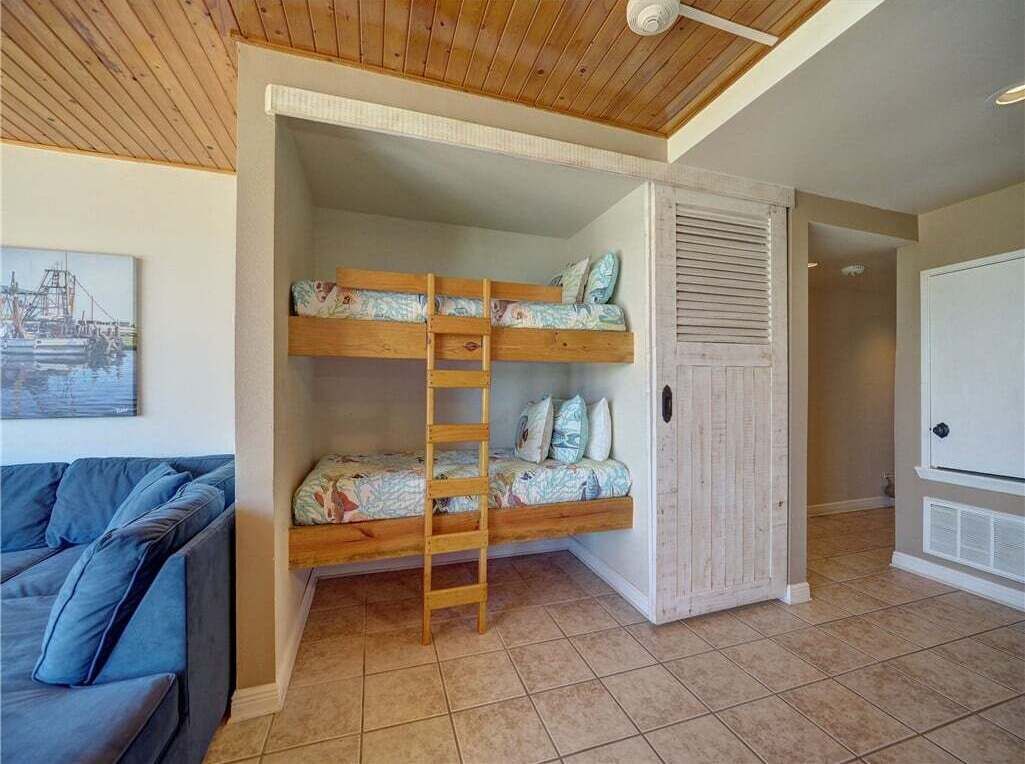 A room with a bunk bed, a ladder, a white wardrobe, and a blue sofa.
