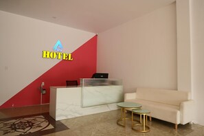 A hotel reception area with a marble reception desk, a red accent wall, a white sofa, and two small round tables. - A Hotel (Da Nang)