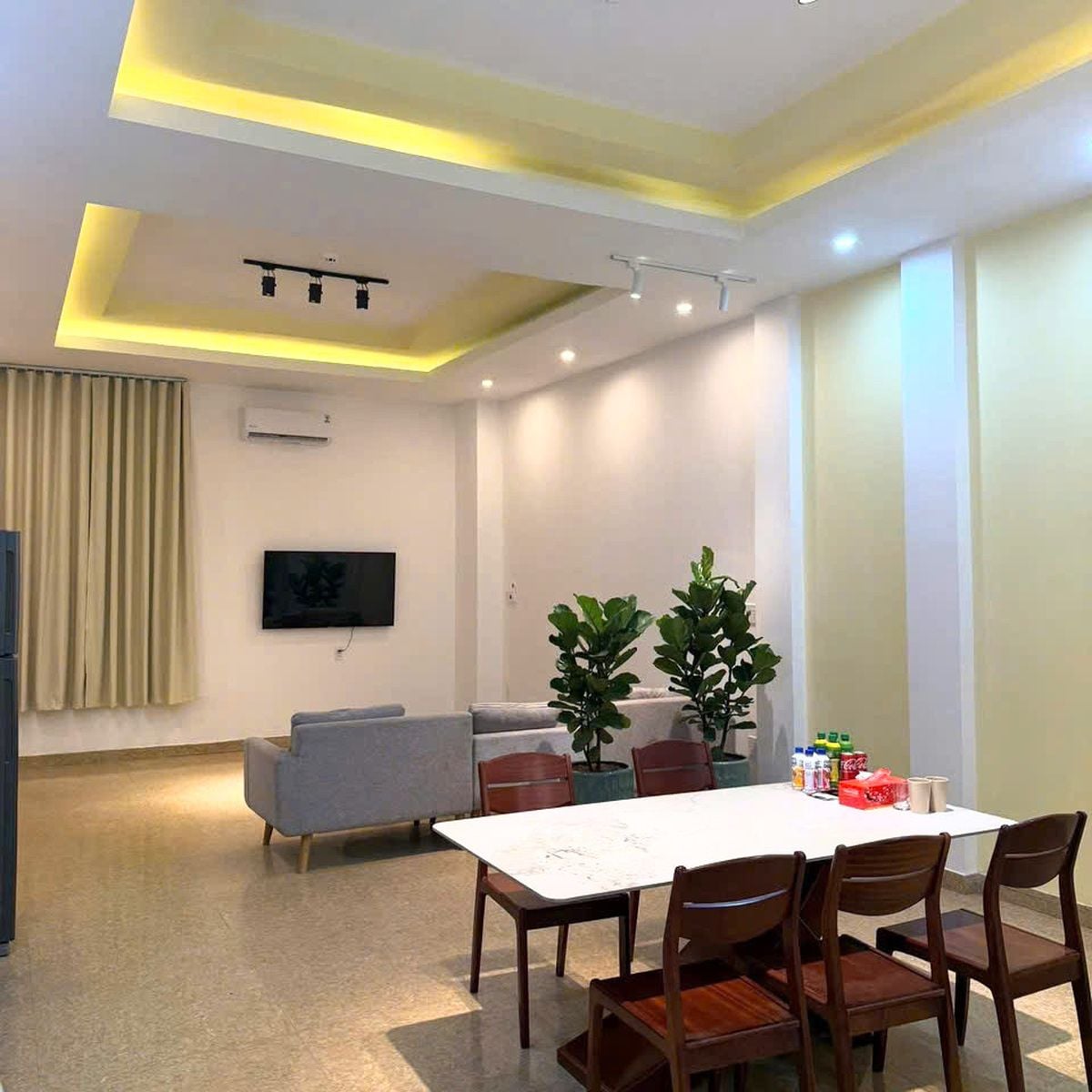 A modern living room with a dining area, a grey sofa, a flat-screen TV, and a ceiling with recessed lighting.