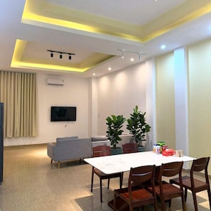 A modern living room with a dining area, a grey sofa, a flat-screen TV, and a ceiling with recessed lighting. - A405 Hotel (Da Nang)