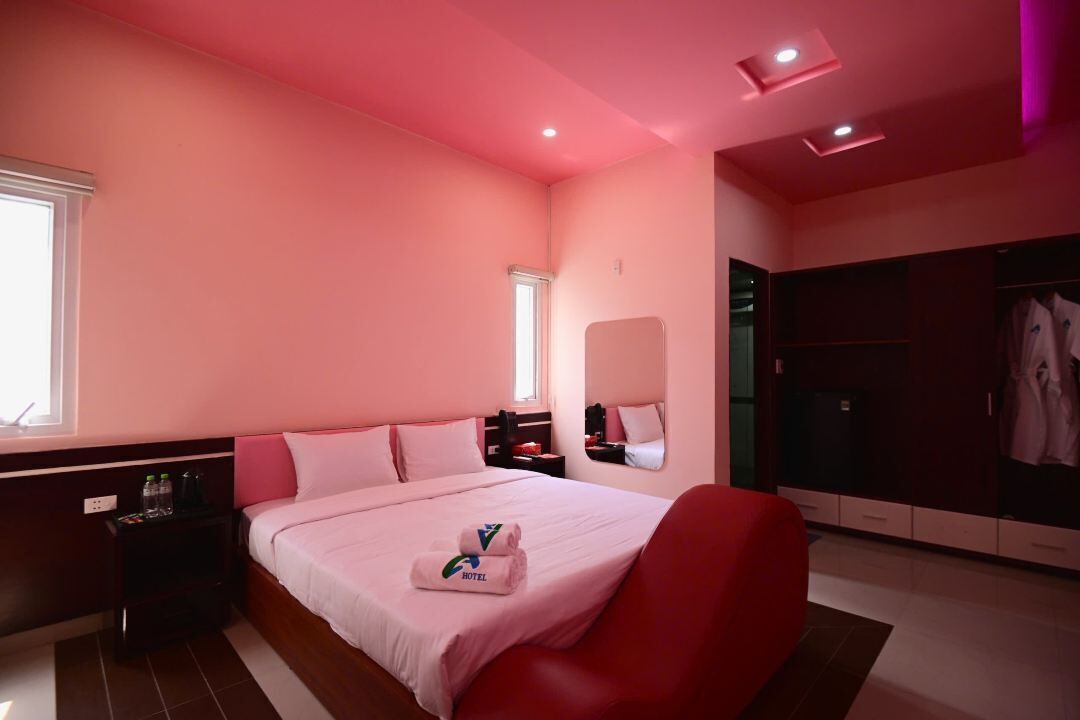 A hotel room with a bed, a red chair, a wardrobe, and a nightstand with a bottle.