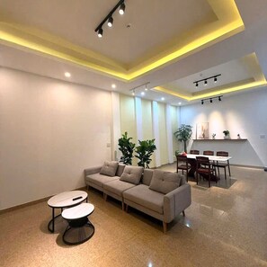A modern living room with a sofa, two tables, and a dining area with chairs. - A Hotel (Da Nang)
