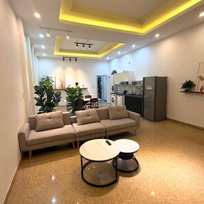 A modern living room with a sofa, two round tables, and a kitchen area in the background. - A Hotel (Da Nang)