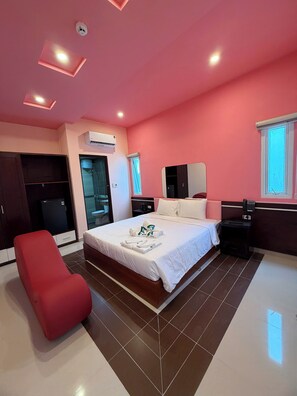 A hotel room with a bed, a red chair, a wardrobe, an air conditioning unit, a bedside table with a phone, and a window with blinds. - A Hotel (Da Nang)