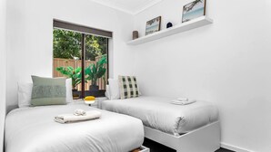 Una camera da letto moderna con due letti, una finestra vista verde e uno scaffale con quadri incorniciati.