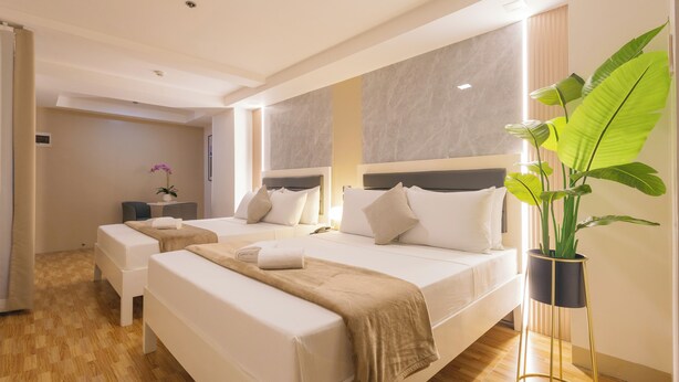 A hotel room with two beds, a bedside table, a potted plant, and a view of the hallway. - Skypark Bay Hotel (Parañaque)