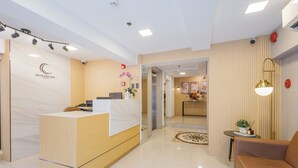 A hotel reception area with a wooden reception desk, a sofa, and a small table with a plant. - Skypark Bay Hotel (Parañaque)