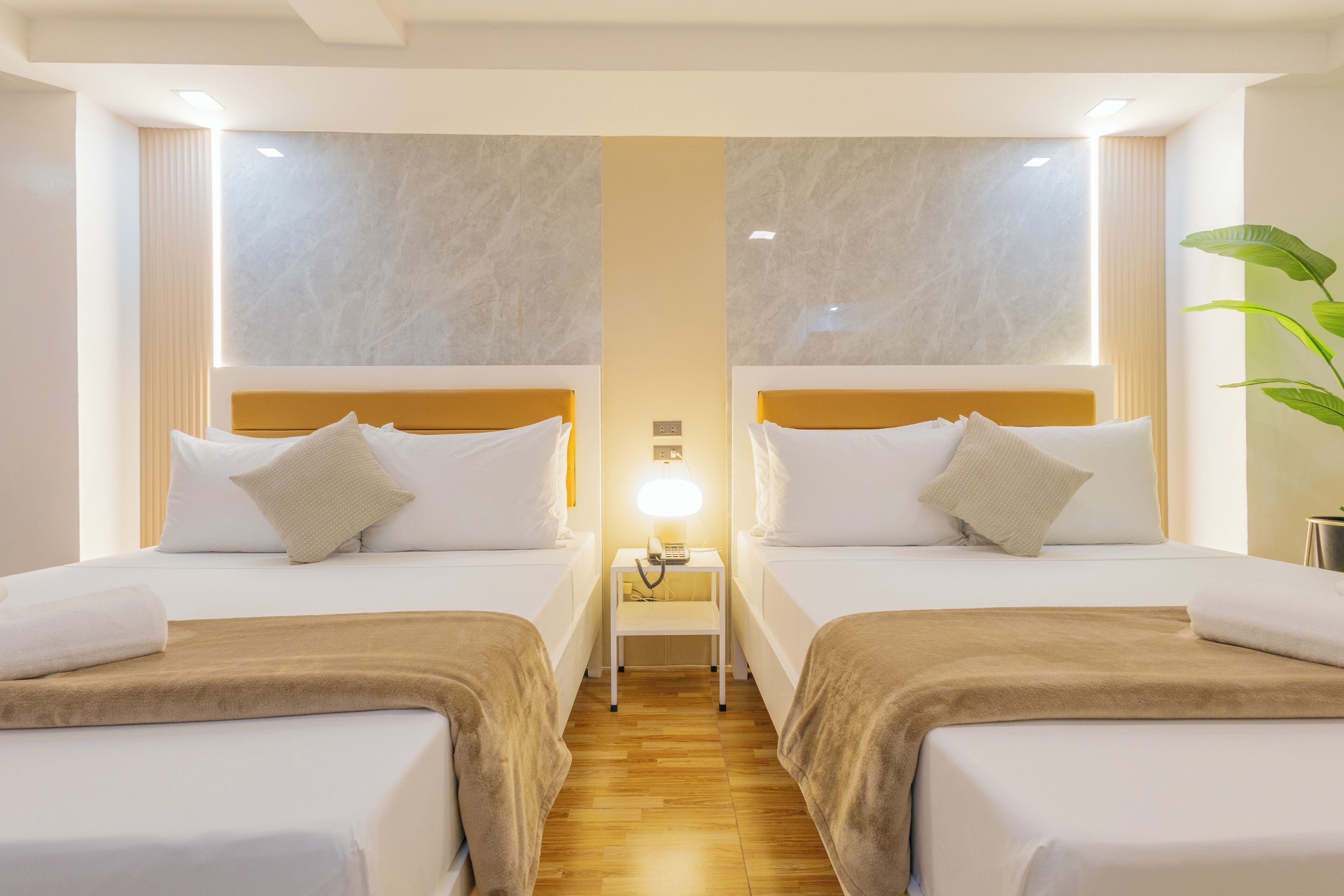 A hotel room with two beds, a nightstand with a lamp, and a large window.