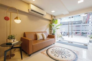 A modern hotel lobby with a brown leather sofa, a round coffee table, a floor lamp, and a large potted plant.