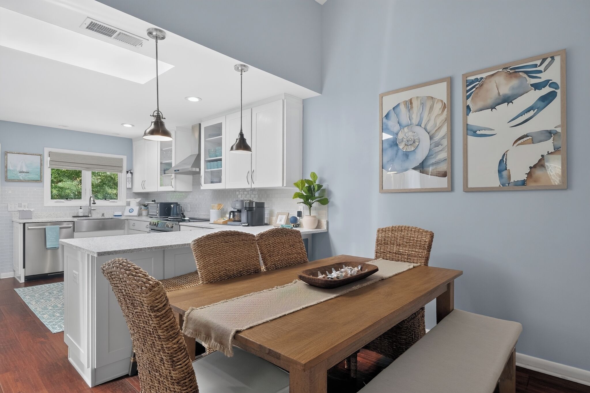 A modern kitchen with white cabinets, a dining area with wicker chairs, and artwork on the walls.