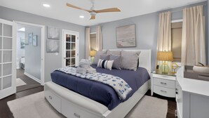 Une chambre à coucher avec un lit, des tables de chevet, un ventilateur de plafond et une vue sur la salle de bain.