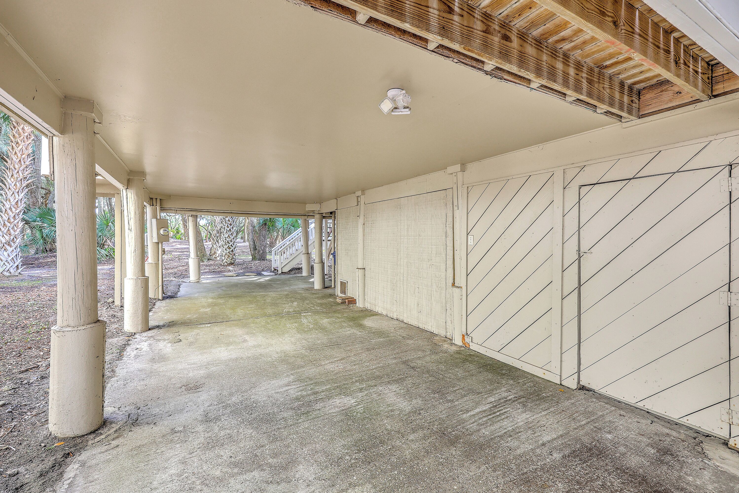 A covered outdoor area with concrete flooring, white pillars, and a wooden ceiling.