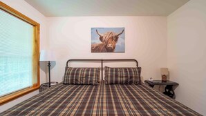 A bedroom with a bed, a lamp, a table, and a painting of a bull on the wall.
