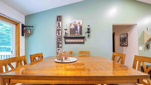 A dining room with a large wooden table, six chairs, and a wall-mounted sign reading "GATHER".