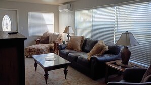 A living room with a dark leather sofa, a glass coffee table, a patterned armchair, and a lamp on a side table. - Beautiful 2/2 Cottage waterfront property on Lake Jackson in Sebring FL. (Sebring)