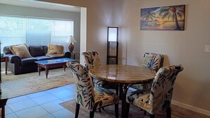 A dining area with a round table and chairs, a sofa with cushions, a lamp, and a painting of a sunset. - Beautiful 2/2 Cottage waterfront property on Lake Jackson in Sebring FL. (Sebring)