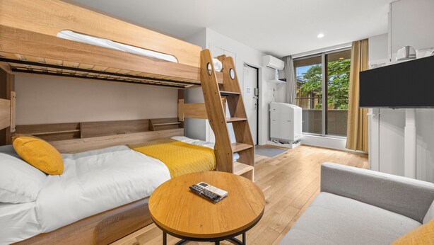 Una habitación de hotel moderna con una litera, una mesa redonda de madera, un sofá y una televisión.