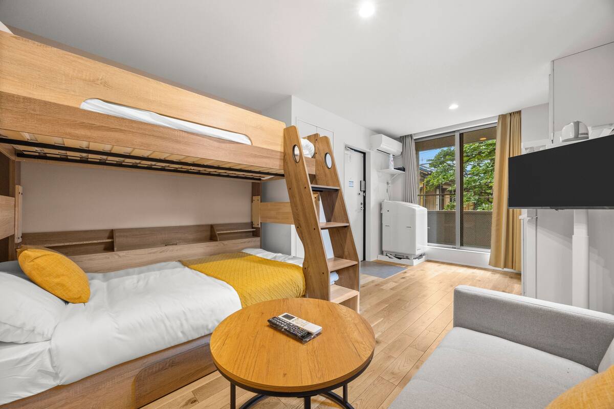 A modern hotel room with a bunk bed, a round wooden table, a sofa, and a television.