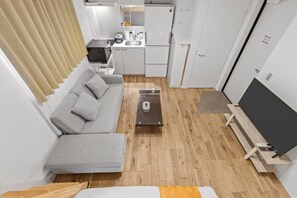 Ein kompakter Wohnraum mit grauem Sofa, einer kleinen Küchenzeile und einem Flachbildfernseher.
