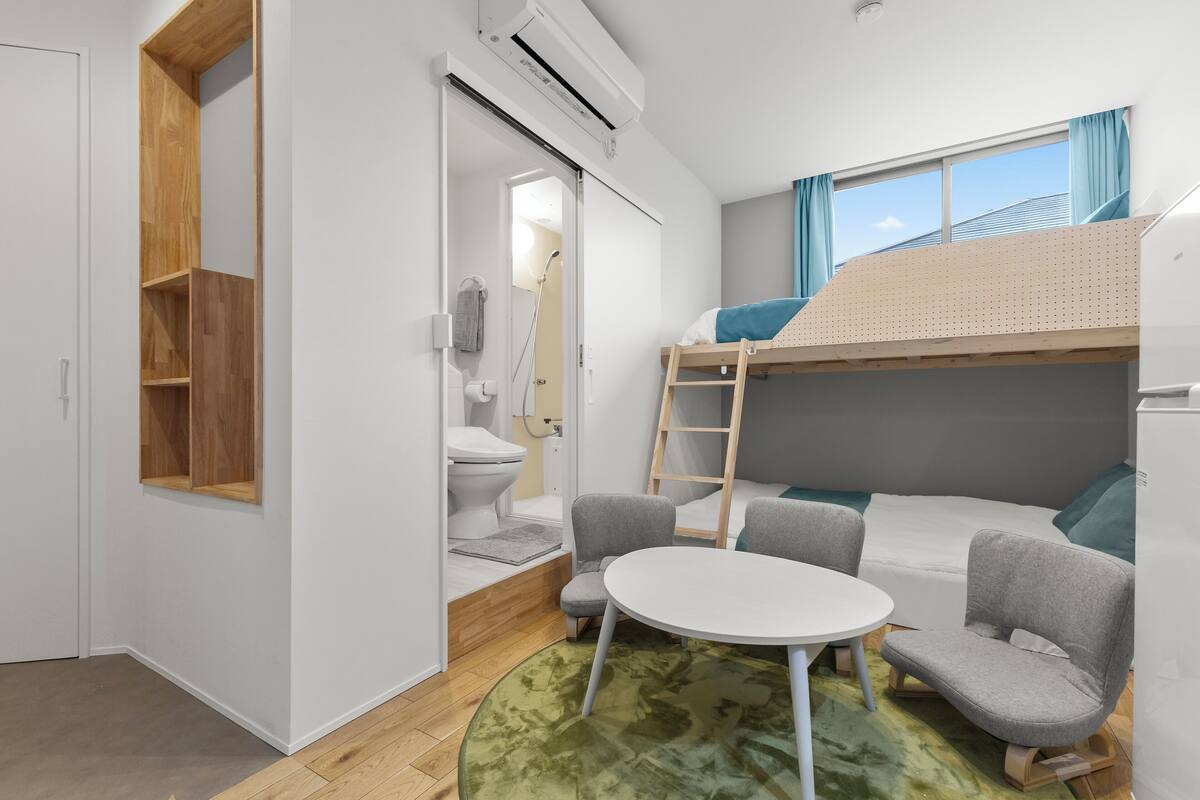 A compact, modern room with a bunk bed, a small table, two chairs, a toilet, and a shower.